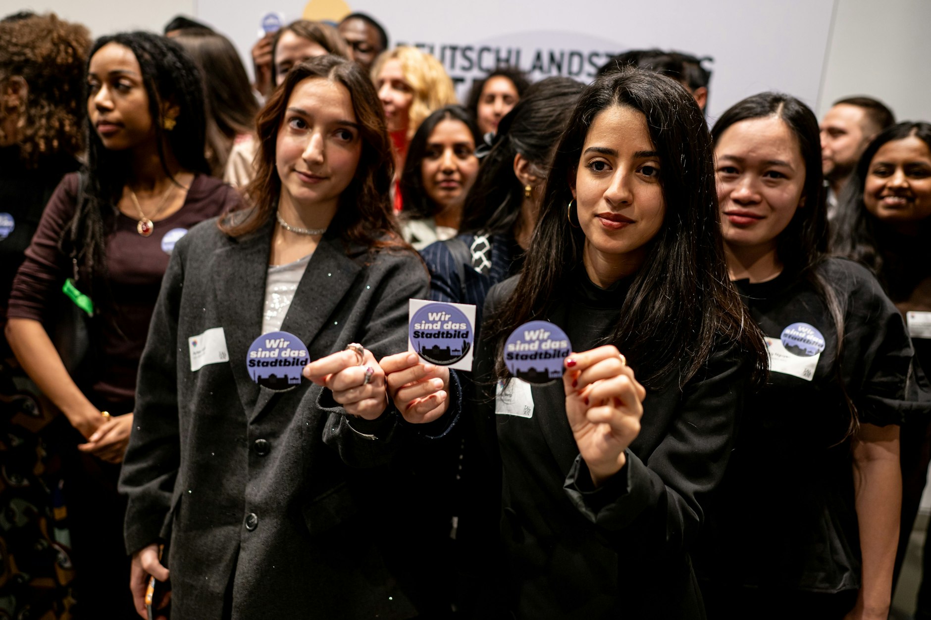 Stipendiaten halten aus Protest bei der Rede des Bundeskanzlers bei Verleihung des Talisman-Preises für gesellschaftlichen Zusammenhalt der Deutschlandstiftung Integration Sticker mit der Aufschrift „Wir sind das Stadtbild“ hoch.