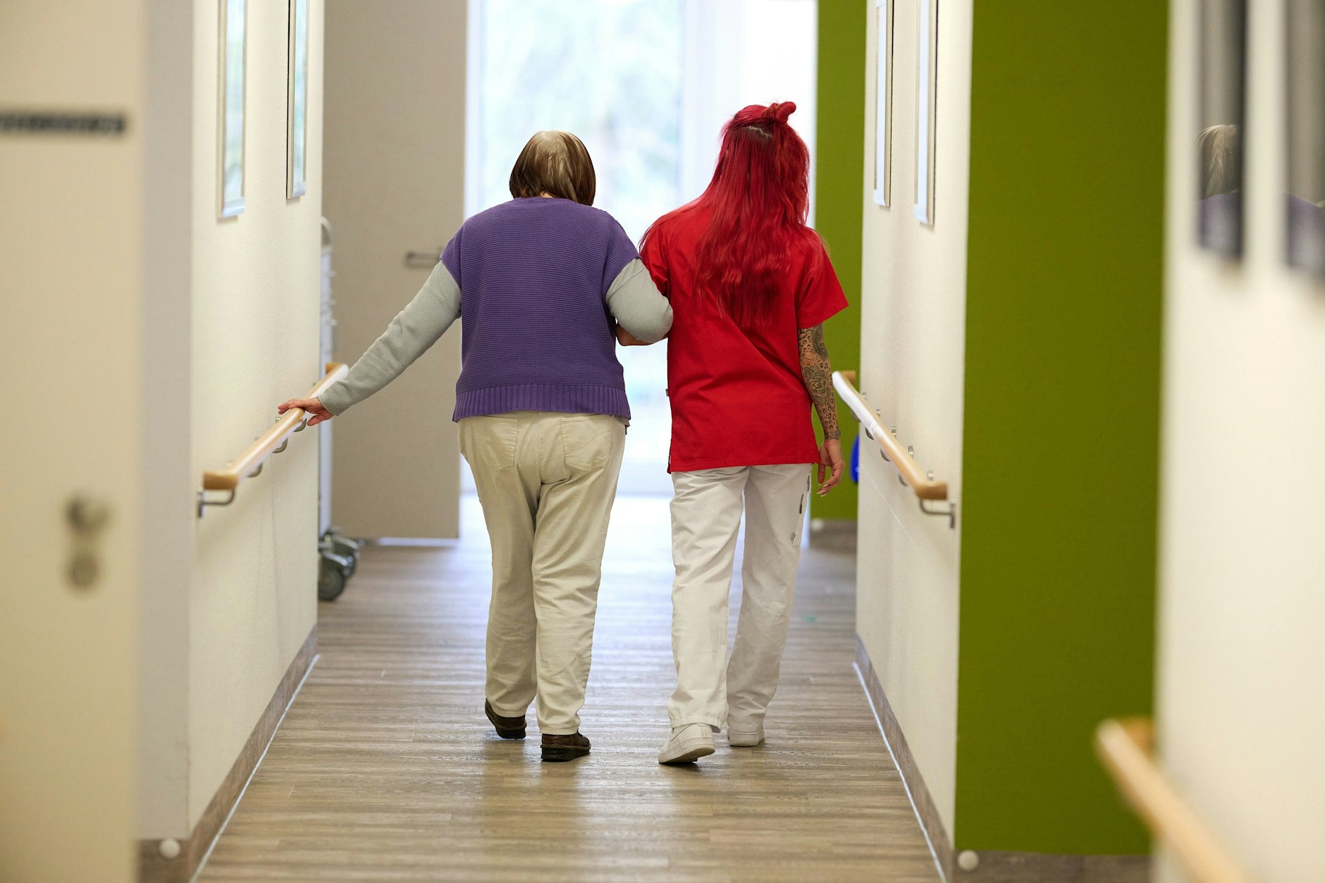 Eine Pflegekraft begleitet in einem Pflegezentrum eine Seniorin über den Flur.