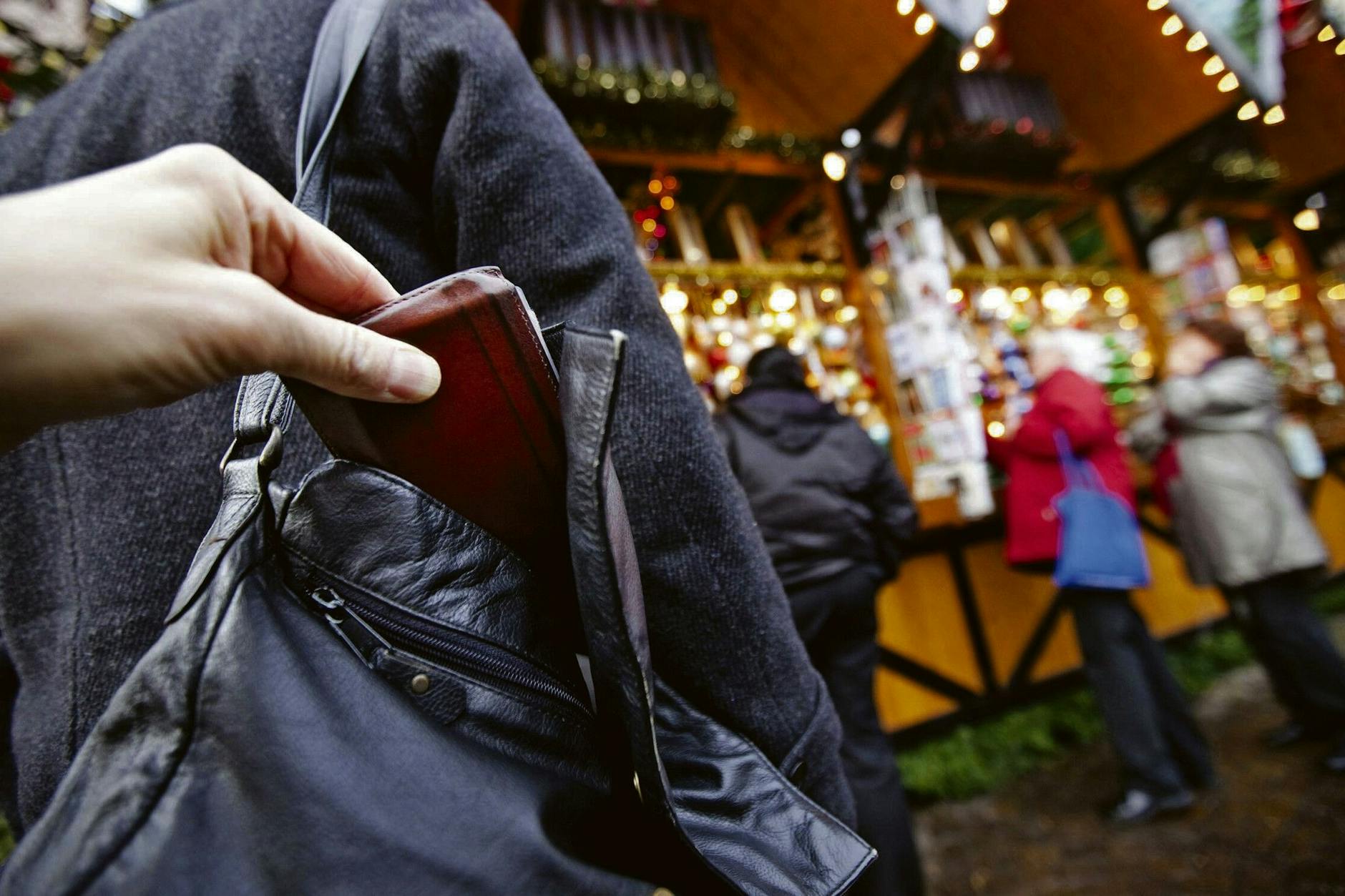 Ein Dieb zieht einer Weihnachtsmarkt-Besucherin die Geldbörse aus der Handtasche (gestellte Szene).