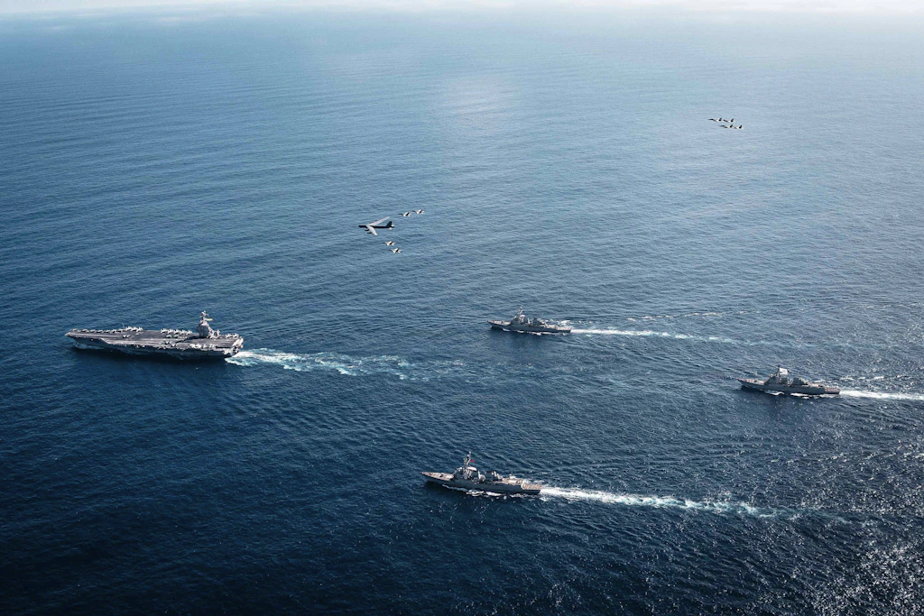 13. November 2025, Karibisches Meer, internationale Gewässer: Luftaufnahme des Flugzeugträgers USS Gerald R. Ford der Ford-Klasse der US-Marine, der eine Formation von Lenkwaffenzerstörern anführt, während ein B-52-Bomber der US-Luftwaffe und Kampfflugzeuge der Marine darüber fliegen