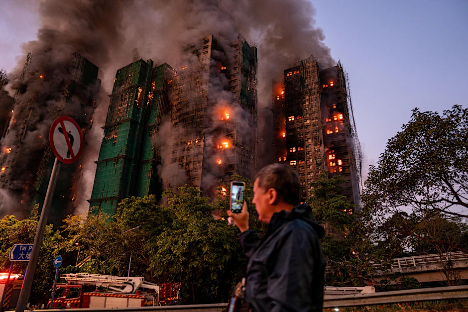 China, Hongkong: Ein Mann nimmt mit seinem Handy Rauch und Flammen auf, als ein Großbrand mehrere Wohngebäude im Wang Fuk Court in Hongkong erfasst.