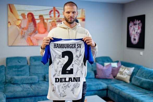 Der ehemalige Fußballspieler Dennis Diekmeier hält in seiner Wohnung ein Trikot des Hamburger SV mit dem Namen seiner ältesten Tochter Delani in den Händen.
