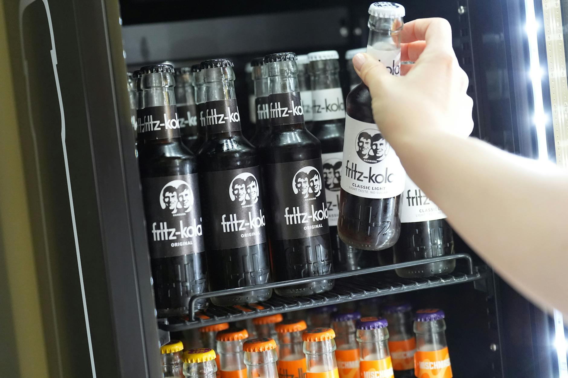 Eine Mitarbeiterin greift nach einer Flasche Fritz-Kola in einem Kühlschrank in der Firmenzentrale der Fritz-Kola GmbH.