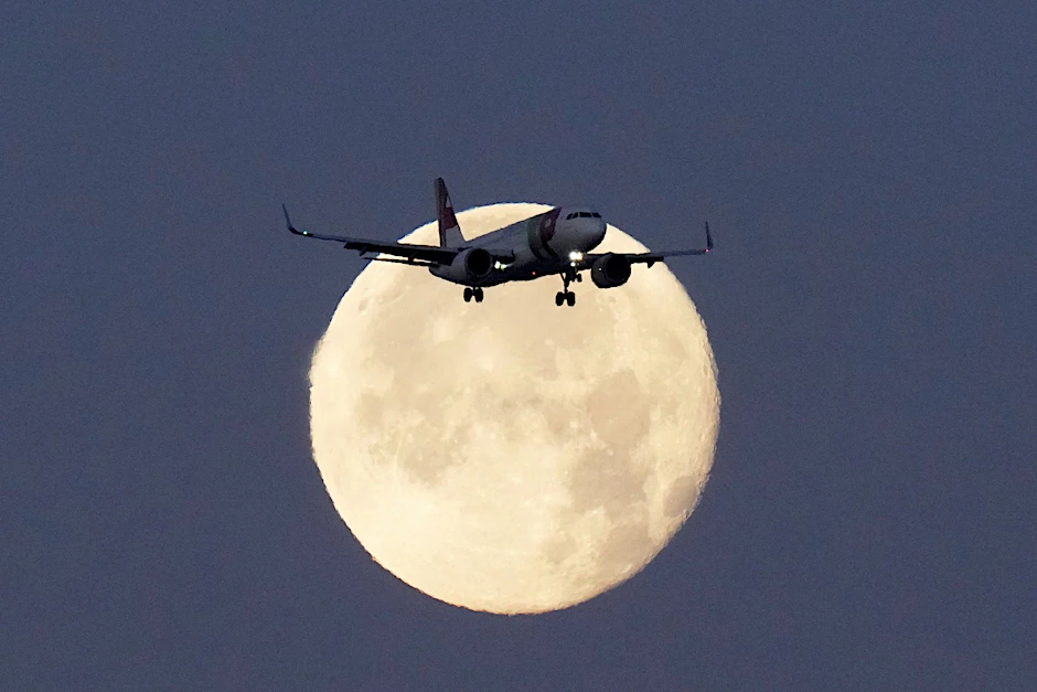 Ein Airbus A320 hebt sich bei Sonnenaufgang gegen den untergehenden Mond ab.