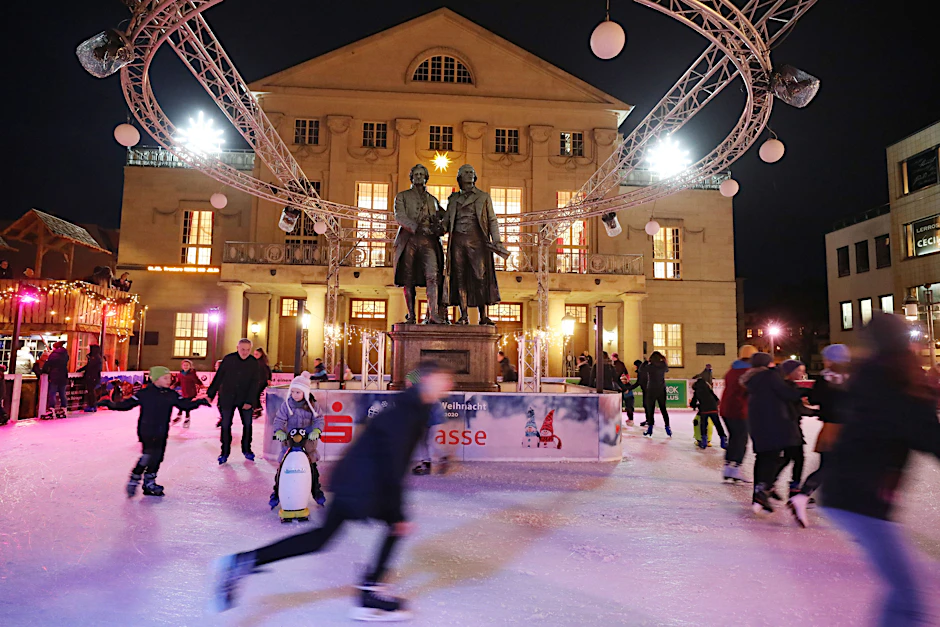 Besucher laufen Schlittschuh auf einer Eisbahn vor dem Deutschen Nationaltheater auf dem Weihnachtsmarkt in Weimar.