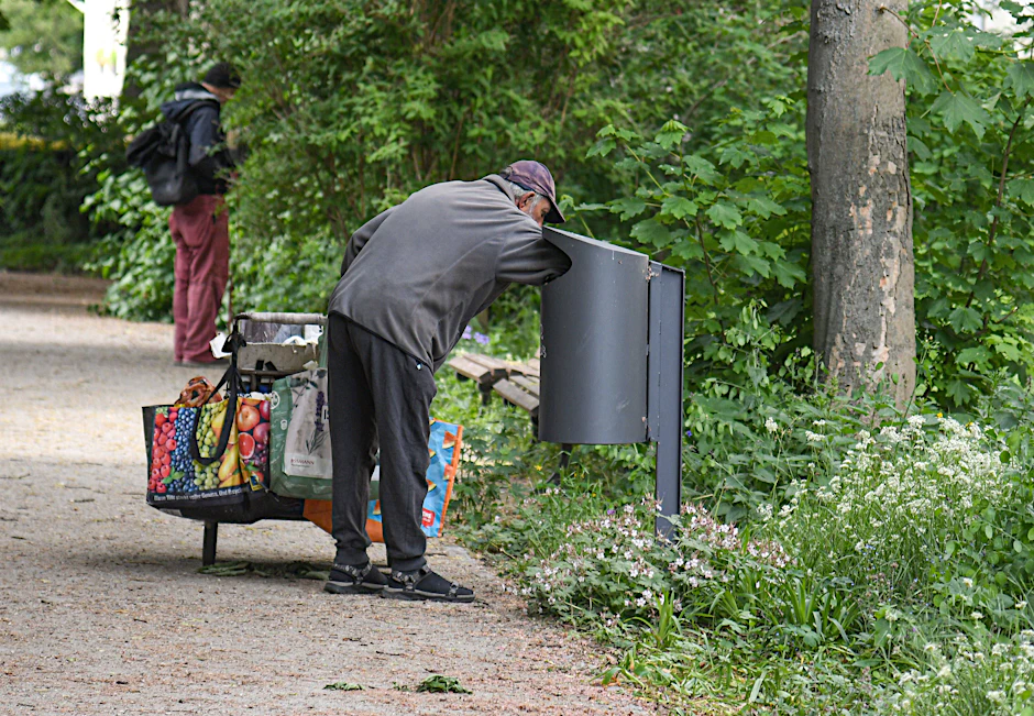 Ein älterer Mann durchsucht einen Abfalleimer in einem Park in Berlin-Friedrichshain nach leeren Flaschen.
