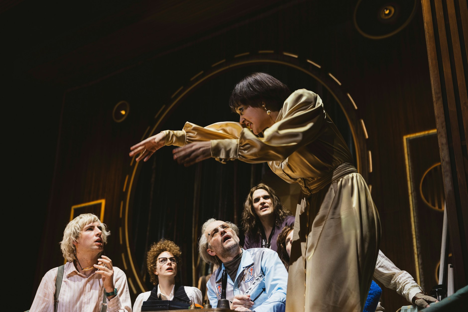 Dr. Crawley (Evamaria Salcher, in Gold) zitiert aus ihrem pornografischen Werk. Die Kollegen Kritiker (Frieder Langenberger, Wiebke Mollenhauer, Moritz Grove und Benjamin Lillie, v.l.) hören zu. Szene aus „Eine Minute der Menschheit“ nach Stanisław Lem im Deutschen Theater