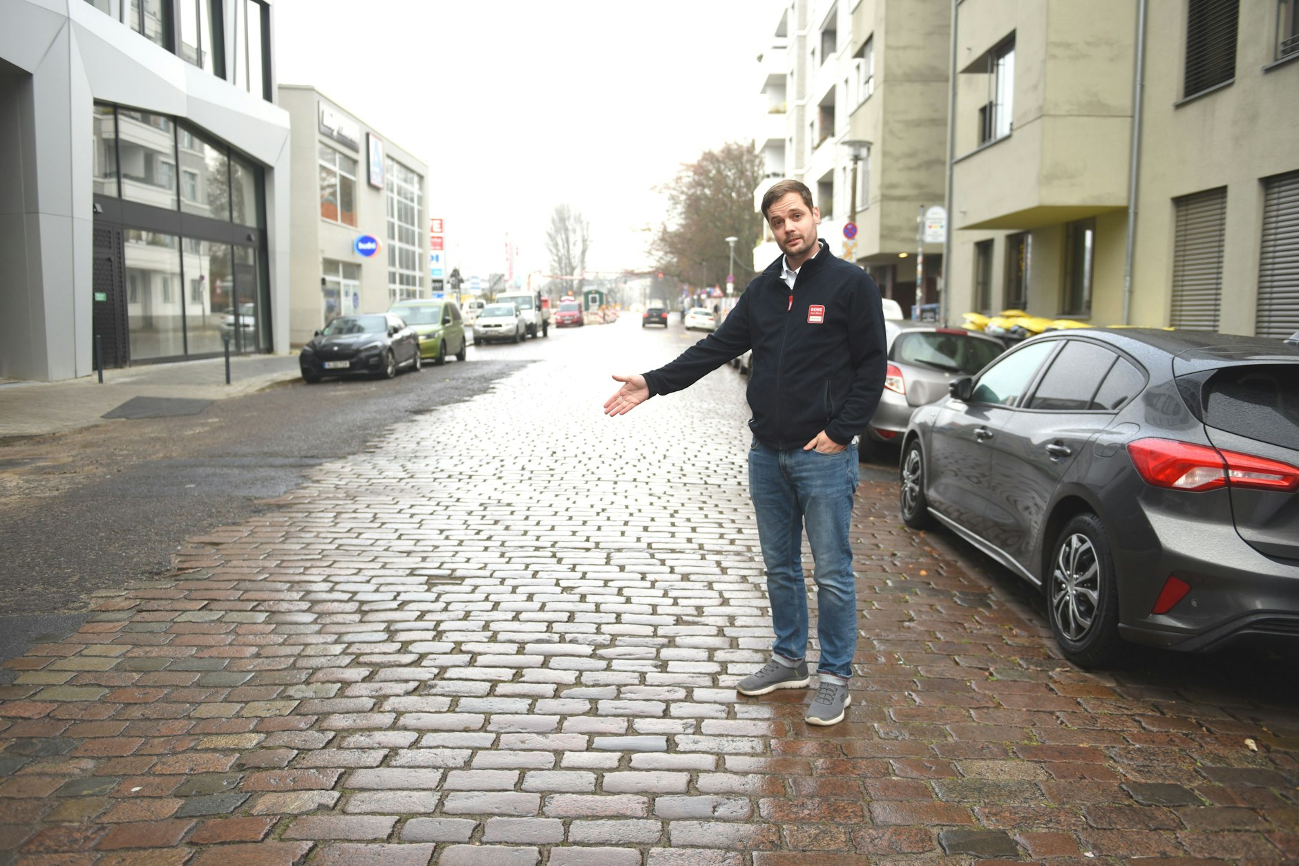 Dennis Henkelmann zeigt, wo die Poller hinkommen. Hinten links befindet sich das Gewerbezentrum, das Rewe gehört.