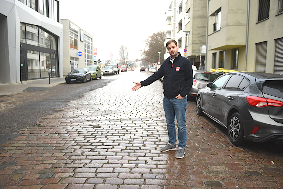 Dennis Henkelmann zeigt, wo die Poller hinkommen. Hinten links befindet sich das Gewerbezentrum, das Rewe gehört.