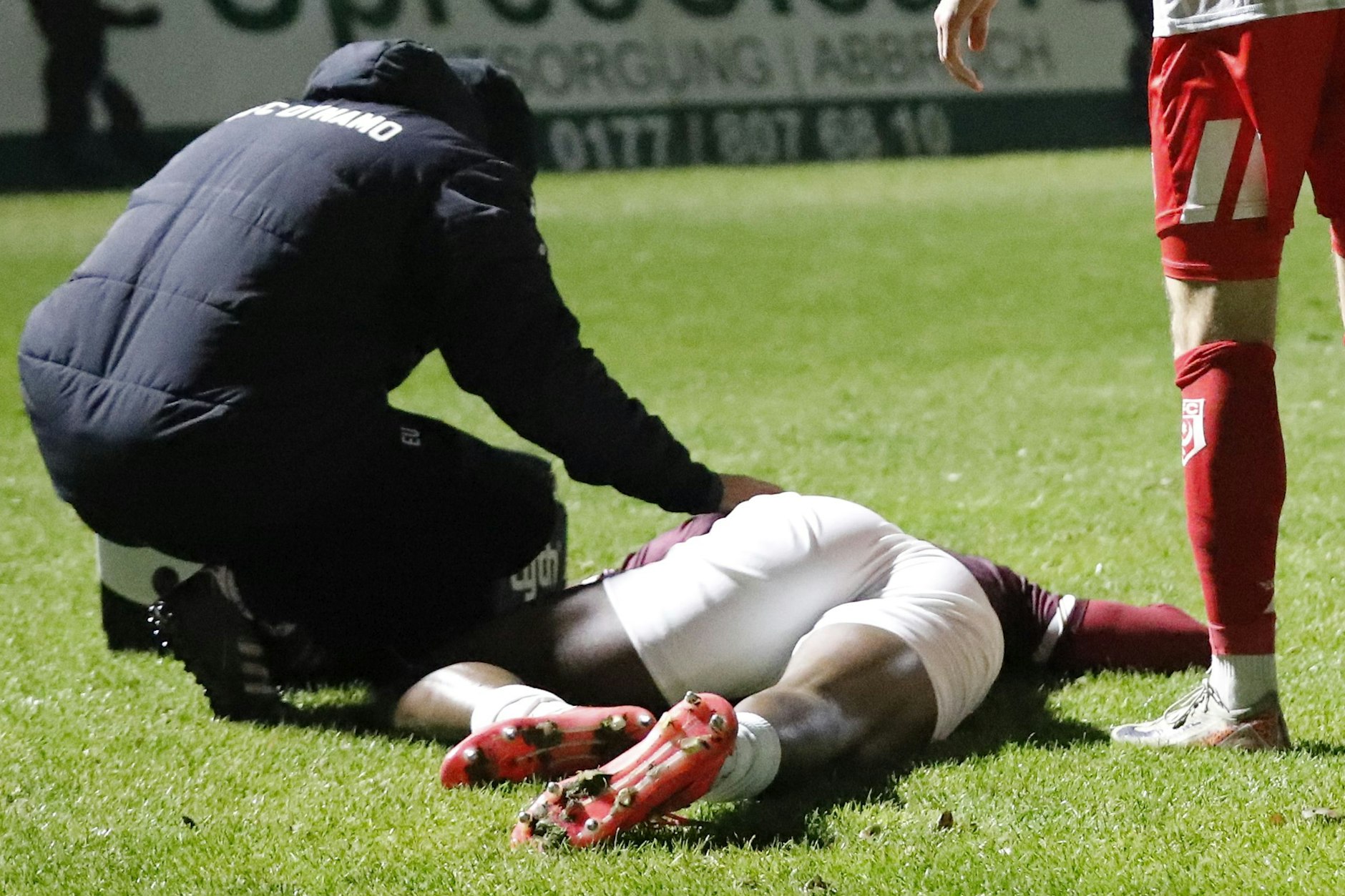 Americo Neves liegt mit Schmerzen am Boden, BFC-Physio Elias Ulsamer ist als erster Helfer beim Dynamo-Pechvogel.