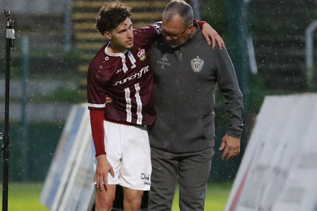 Can Karatas erwischte es gegen den Greifswalder FC. Auf BFC-Teammanager Jörn Lenz gestützt zeigt er, wo die Schmerzen sind.