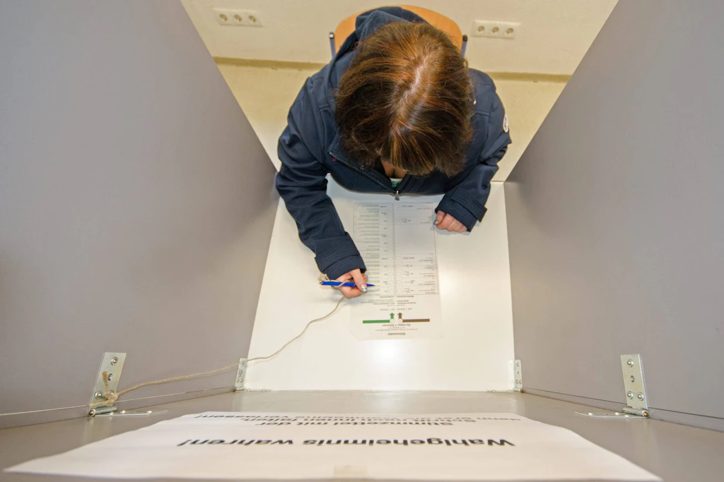 Eine Frau sitzt in einer Wahlkabine und betrachtet den Wahlschein.