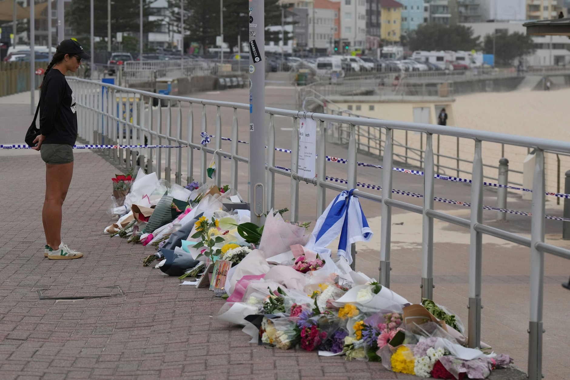 Eine Frau steht am Bondi Beach vor abgelegten  Blumen in Gedenken an die Getöteten.