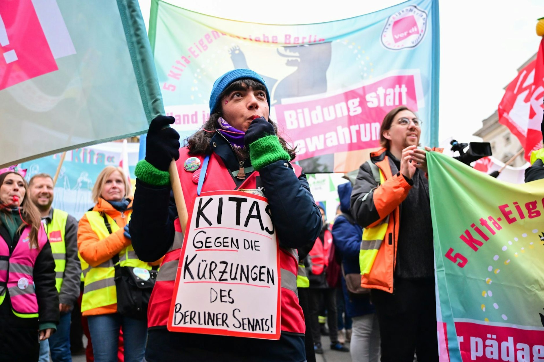 Eine Streikende vor dem Abgeordnetenhaus mit einem Schild, auf dem „Kitas gegen die Kürzungen des Berliner Senats!“ steht.