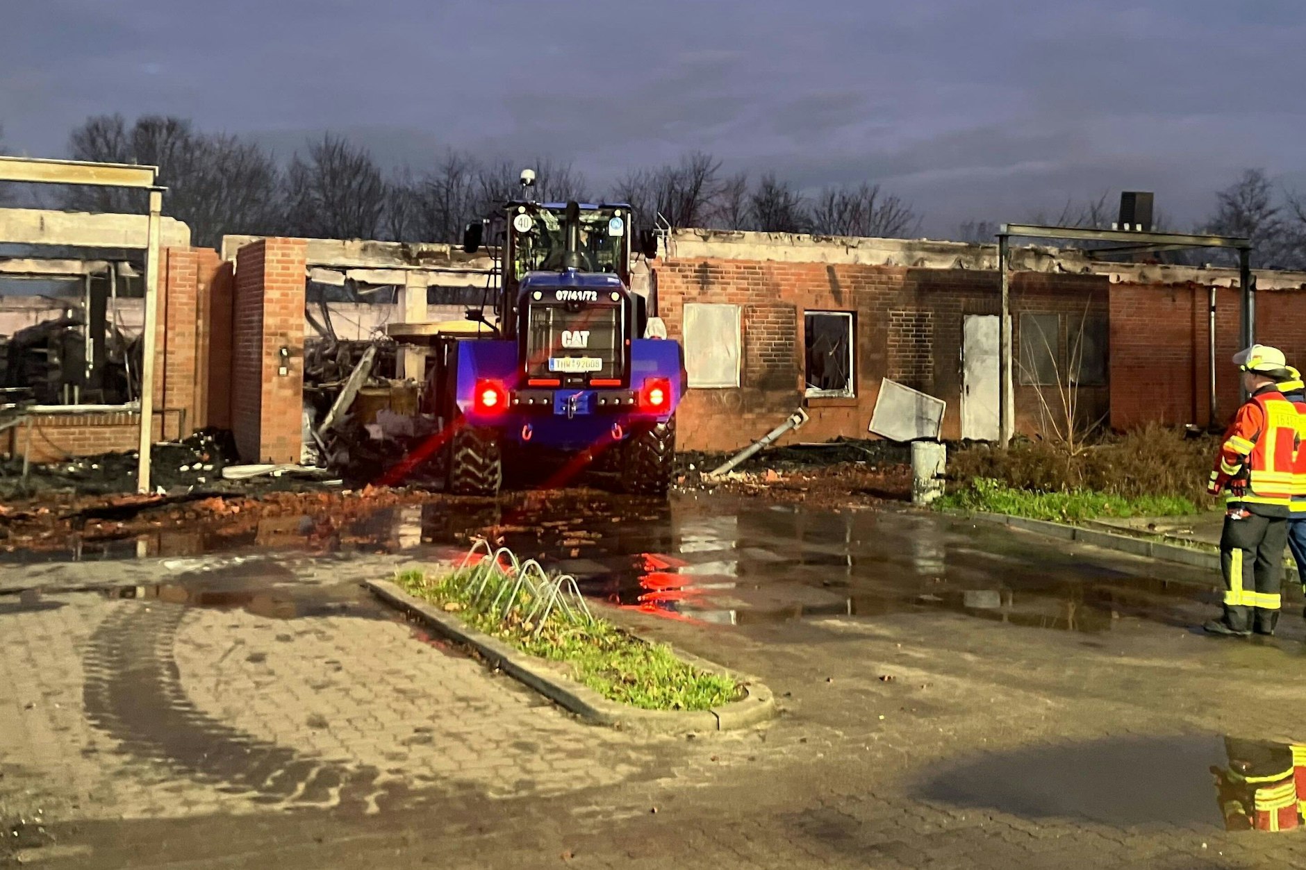 Nach dem Großbrand sichern Einsatzkräfte das ausgebrannte Gebäude in Zehdenick, während schwere Technik Trümmer beseitigt.