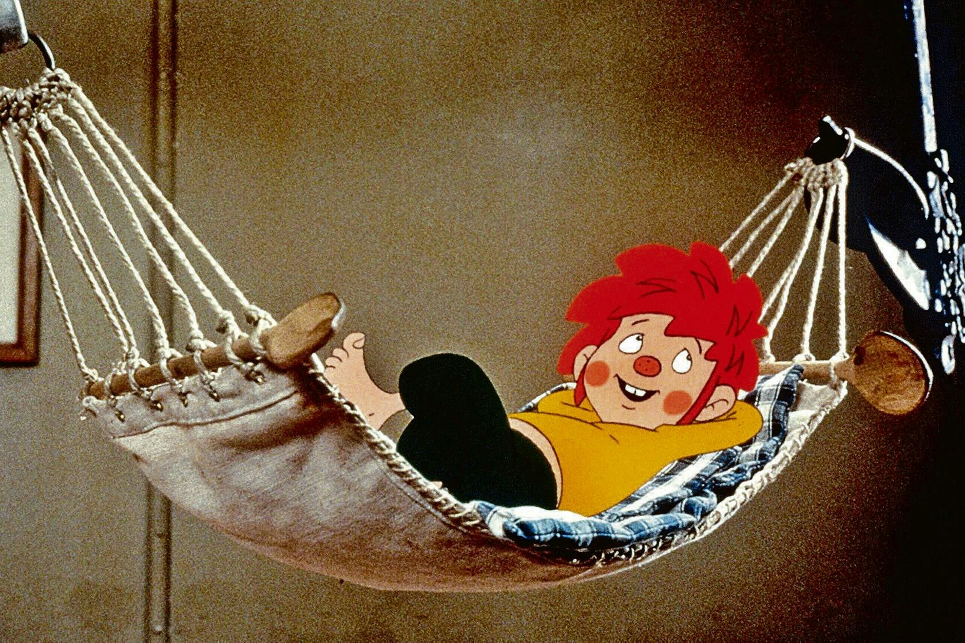 Pumuckl entspannt in einer Hängematte. Der freche Kobold mit den roten Haaren begeistert seit über 60 Jahren Generationen von Fans.