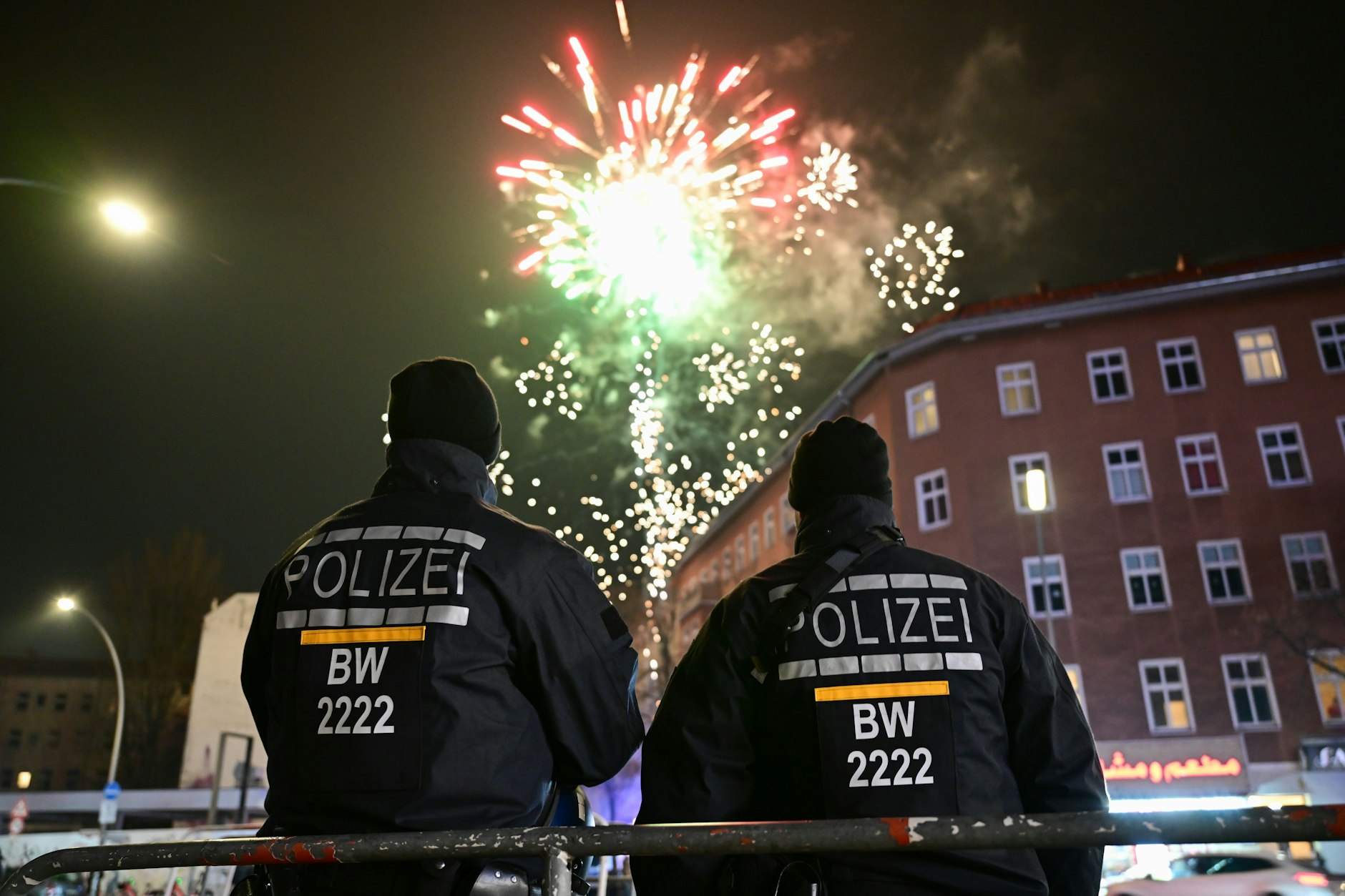 Polizeibeamte schauen während der Silvesternacht an der Sonnenallee auf Feuerwerk, das knapp außerhalb der Verbotszone abgefeuert wird.