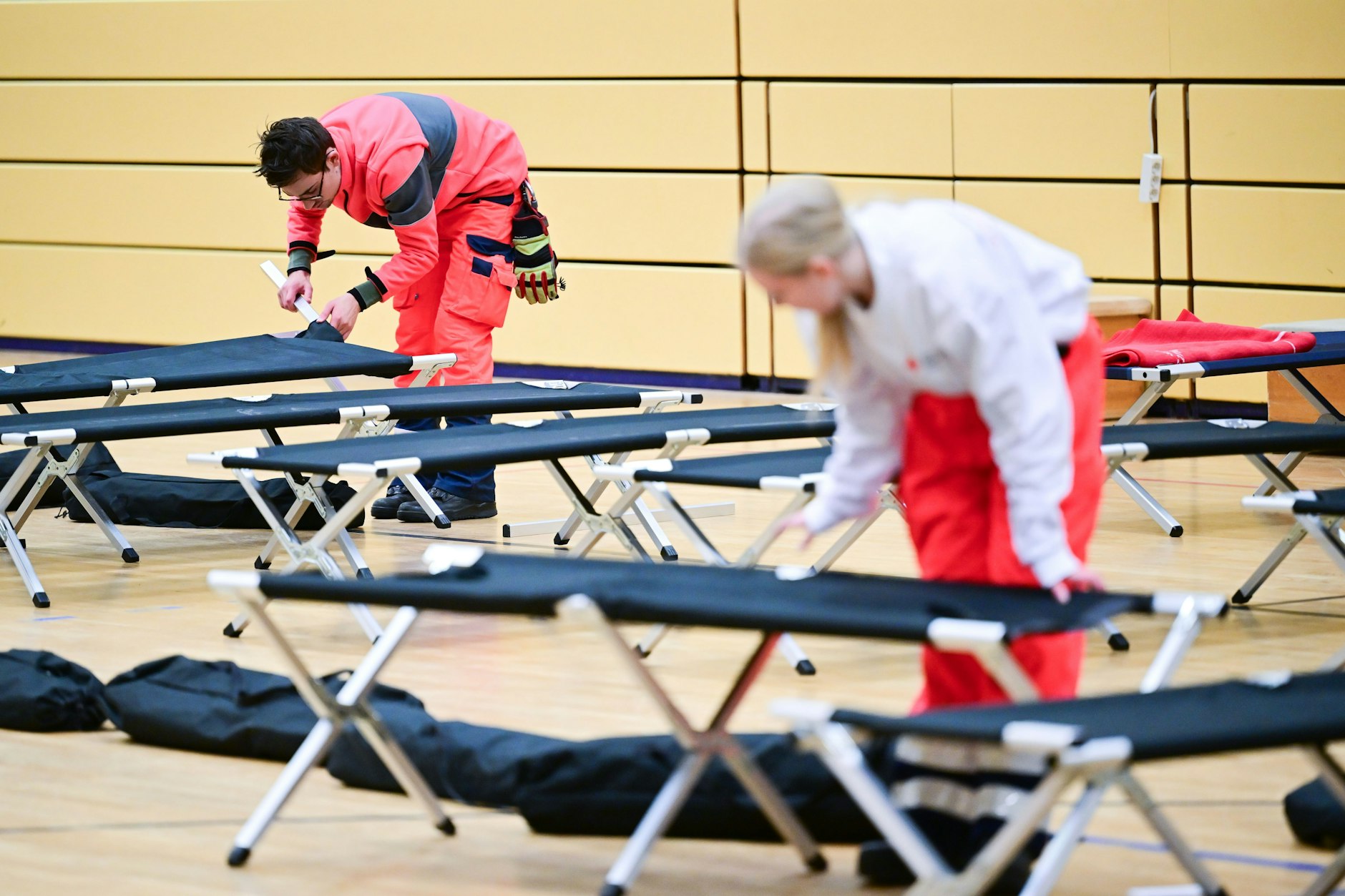 Ehrenamtliche Mitarbeiter des DRK bauen in einer Notunterkunft Feldbetten auf. 