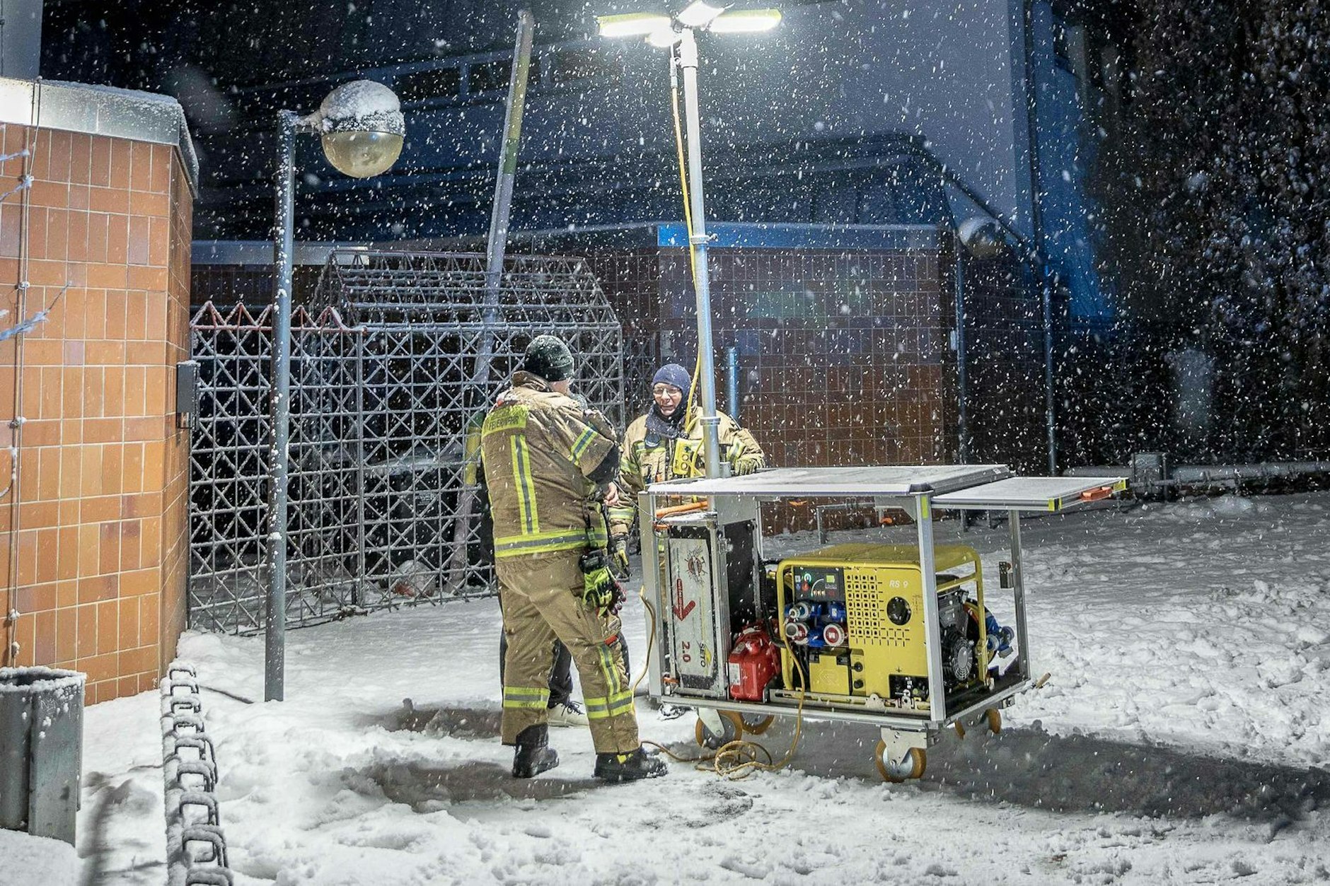 Einsatzkräfte der Berliner Feuerwehr stehen vor einem Generator-Lichtmast an einer Katastrophenschutz-Kontaktstelle vor der Carl-Schuhmann-Sportanlage in Berlin-Lichterfelde.