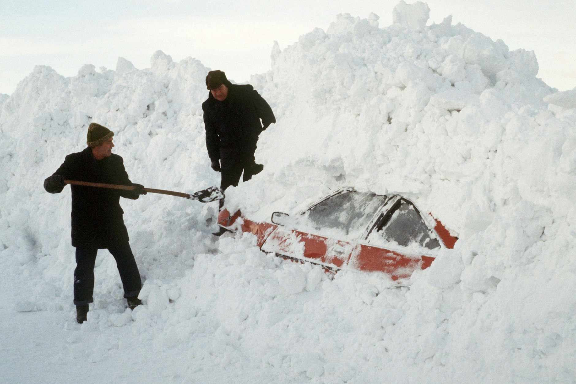 Der Norden Deutschlands ist unter Schneemassen begraben. Zwei Männer graben in Schleswig-Holstein mit einer Schaufel ein Auto aus.