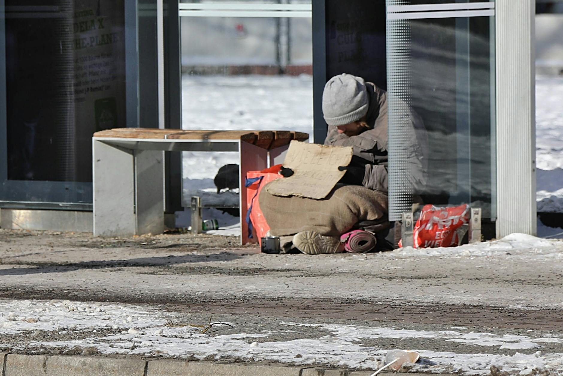 Ein Obdachloser kauert bei Schnee und frostigen Temperaturen an einer Bushaltestelle.