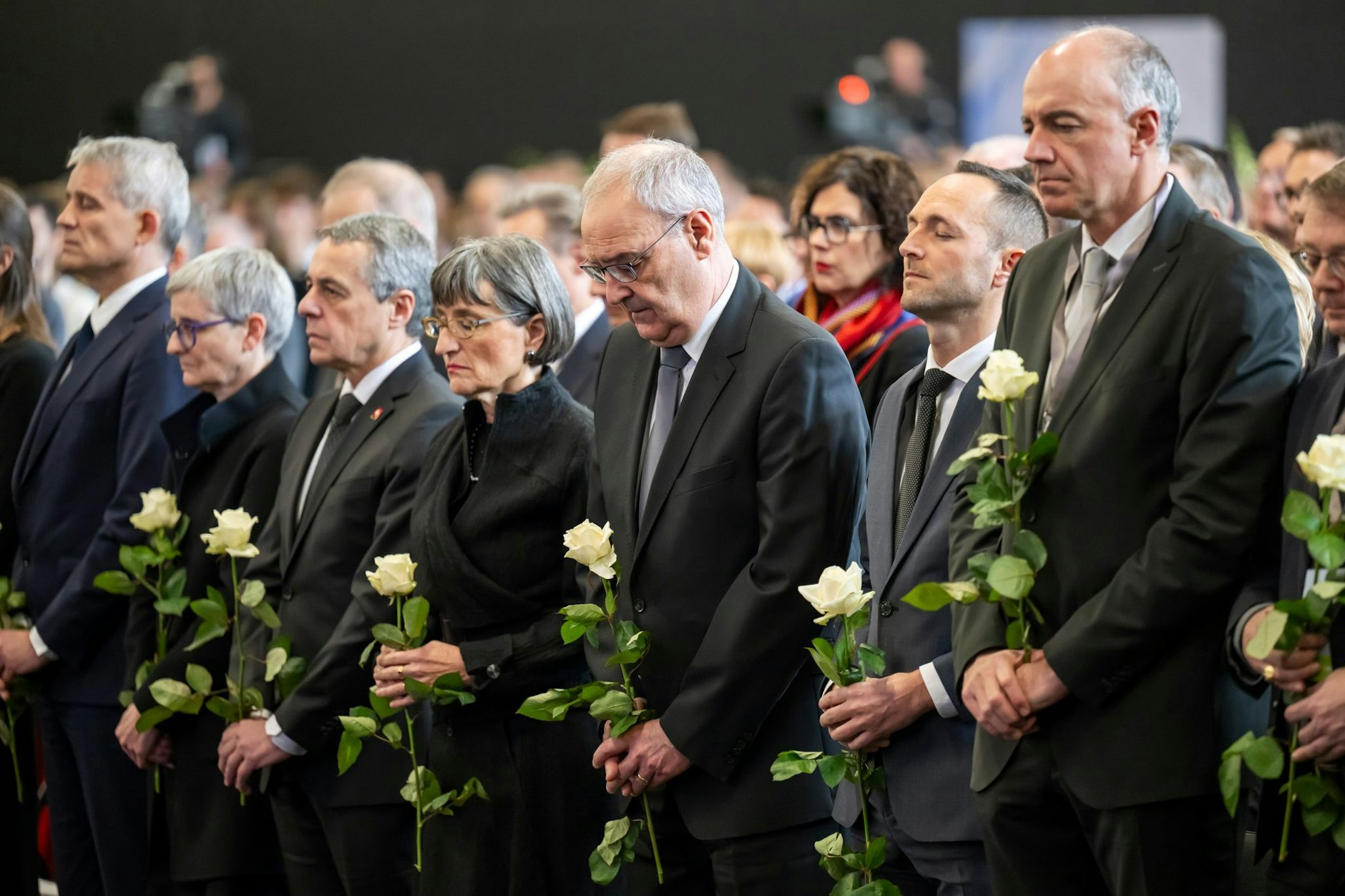 Bundesrat Beat Jans (v.l.n.r.), Bundesrat und Außenminister Ignazio Cassis und seine Frau Paola Cassis, Bundespräsident Guy Parmelin und seine Frau Caroline Parmelin, Mathias Reynard, Staatsrat und Präsident des Staatsrates des Kantons Wallis, Christophe Darbellay, Staatsrat des Kantons Wallis, und Franz Ruppen, Staatsrat des Kantons Wallis, legen eine Schweigeminute ein, während der Trauerfeier am Freitag.