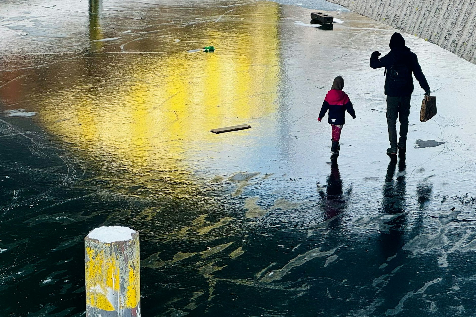 Eine Person und ein Kind gehen über die vereiste Wasserfläche des Neuköllner Schifffahrtskanals am Weigandufer unter der Treptower Brücke.