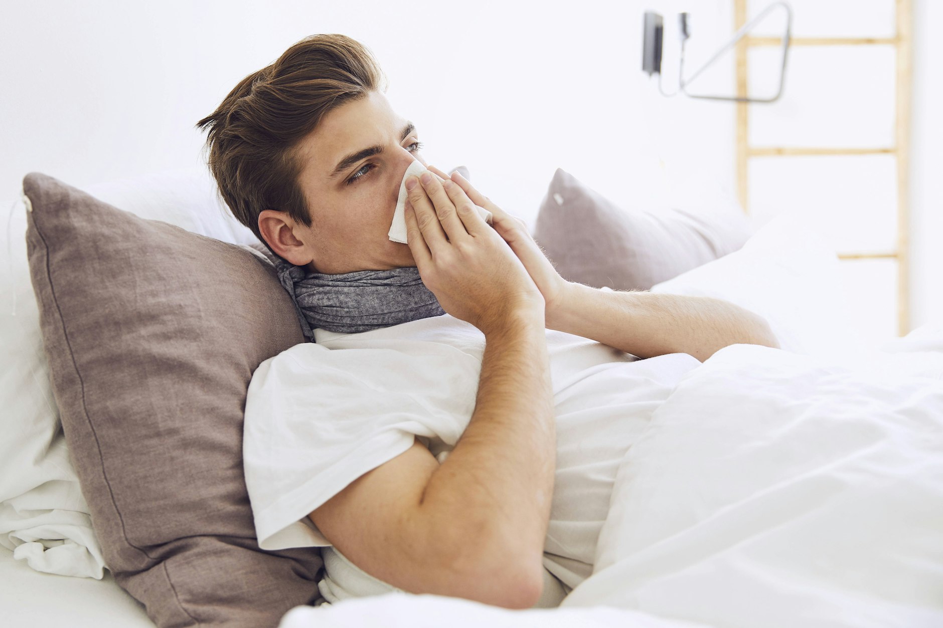Ein Influenza-Patient liegt im Bett und putzt sich die Nase.