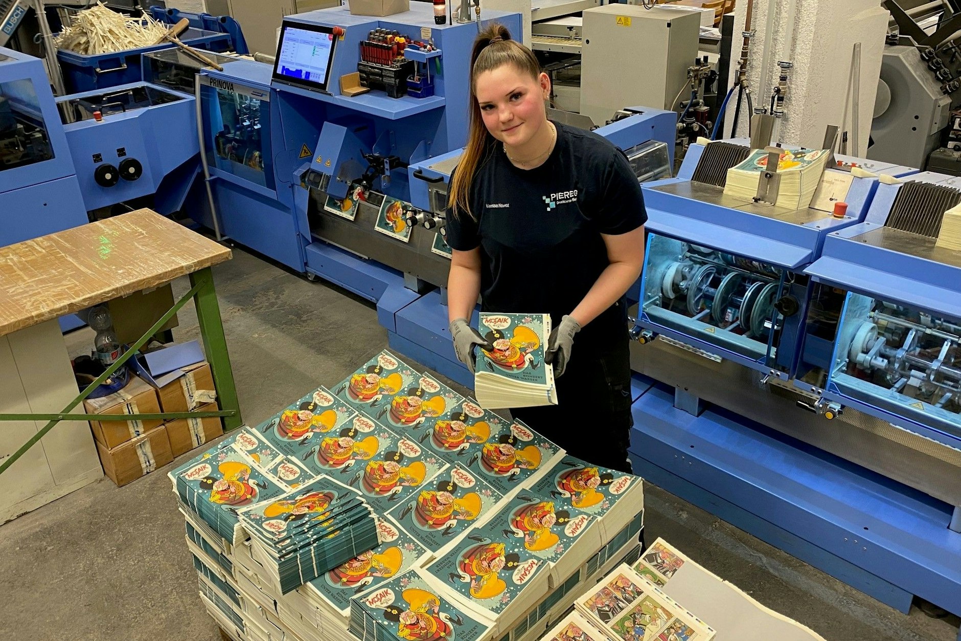 Auszubildende Vanessa Nowrat (18) steckt die letzten Mosaik-Hefte in die Maschine, wo sie geschnitten und geheftet werden.