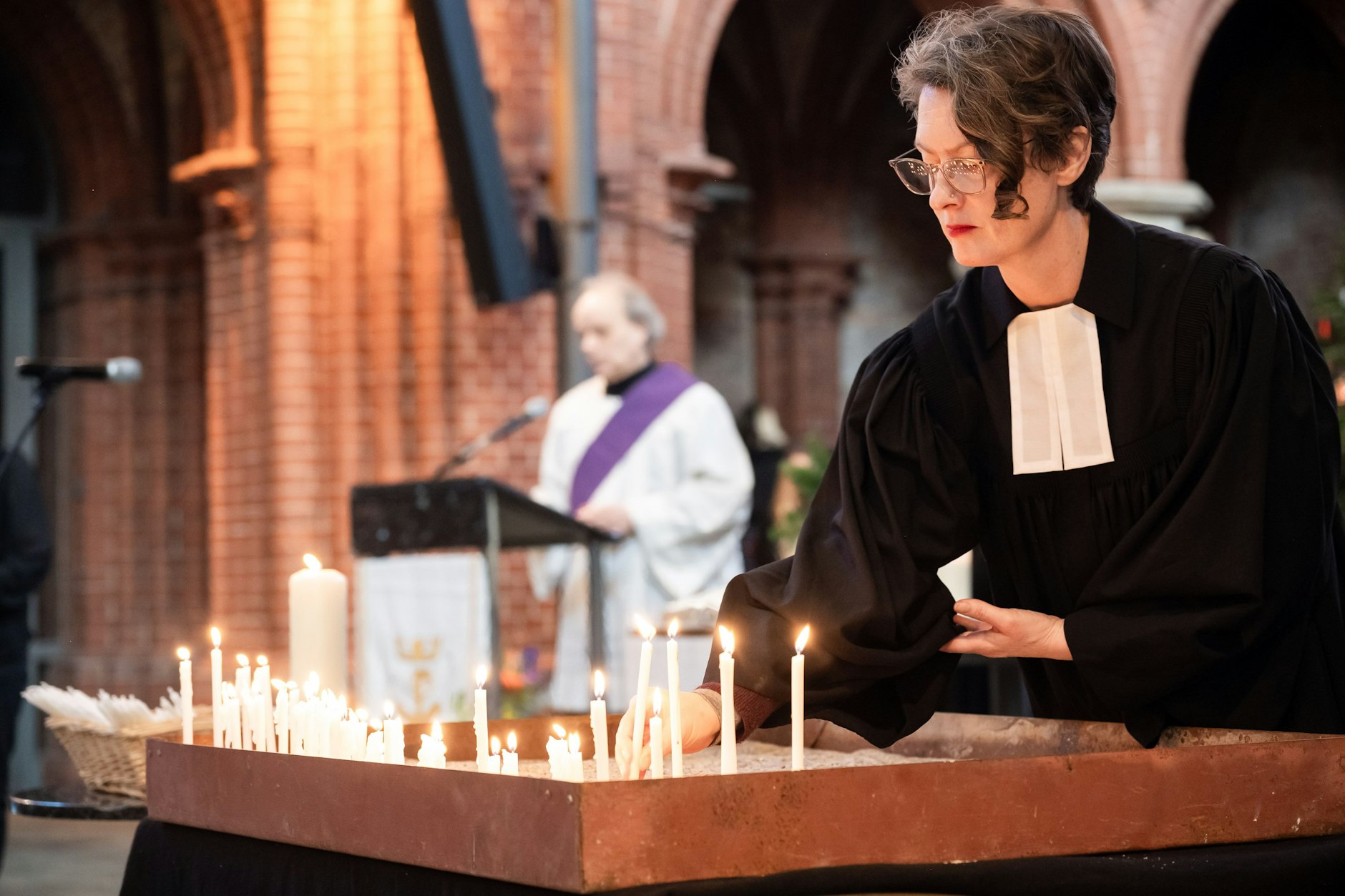Pfarrerin Christina Biere (r.) zündet während der Trauerfeier eine Kerze an.