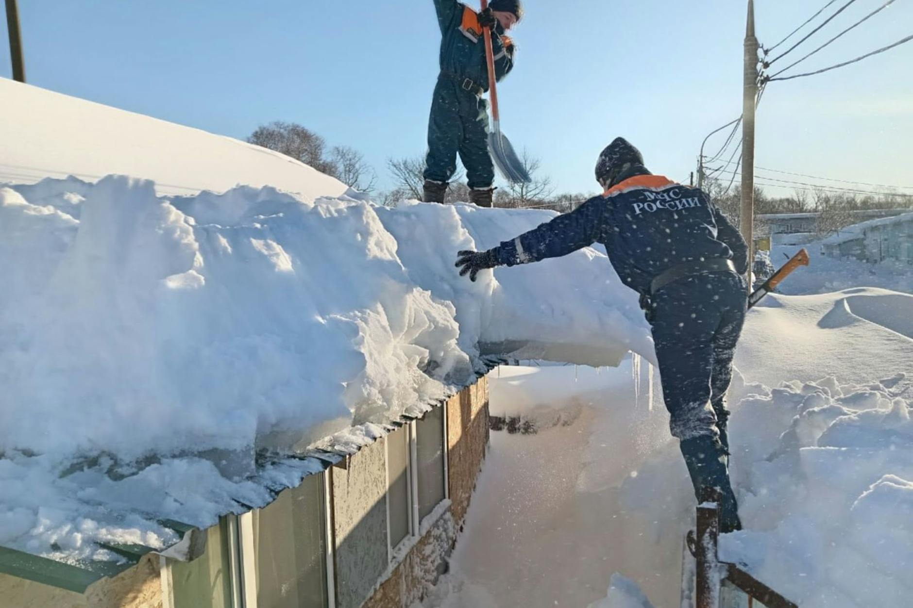Einsatzkräfte räumen Schnee von einem Dach, um Dachlawinen zu verhindern.