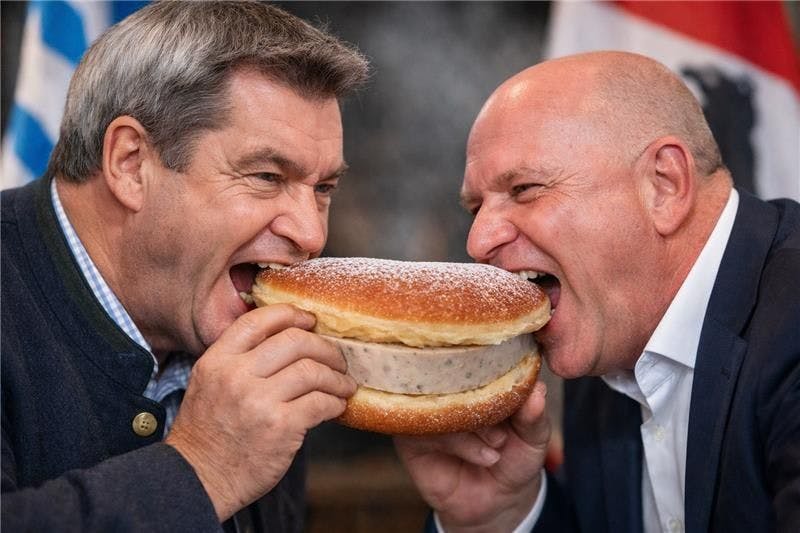 Ist der Weißwurst-Pfannkuchen kulinarische Völkerverständigung? So stellt es sich die KI vor: Bayerns Ministerpräsident Markus Söder und Berlins Regierender Bürgermeister Kai Wegner beißen in das Gebäck.