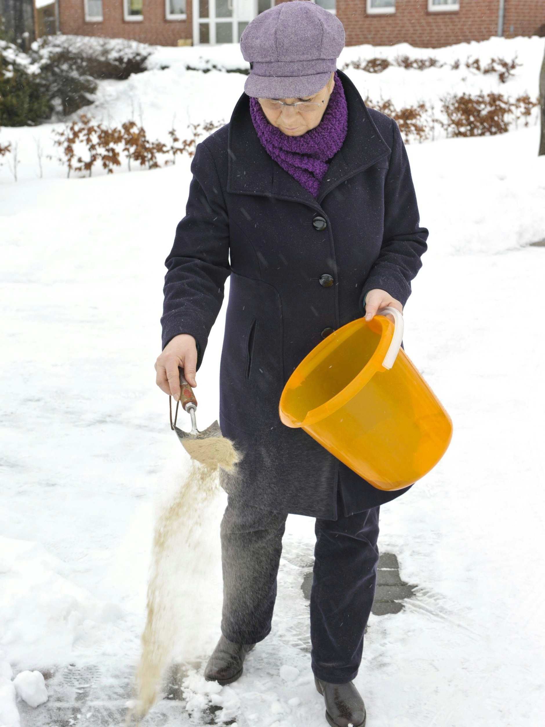 Eine Frau streut einen Gehweg - bei der BSR gibt es Granulat kostenlos.