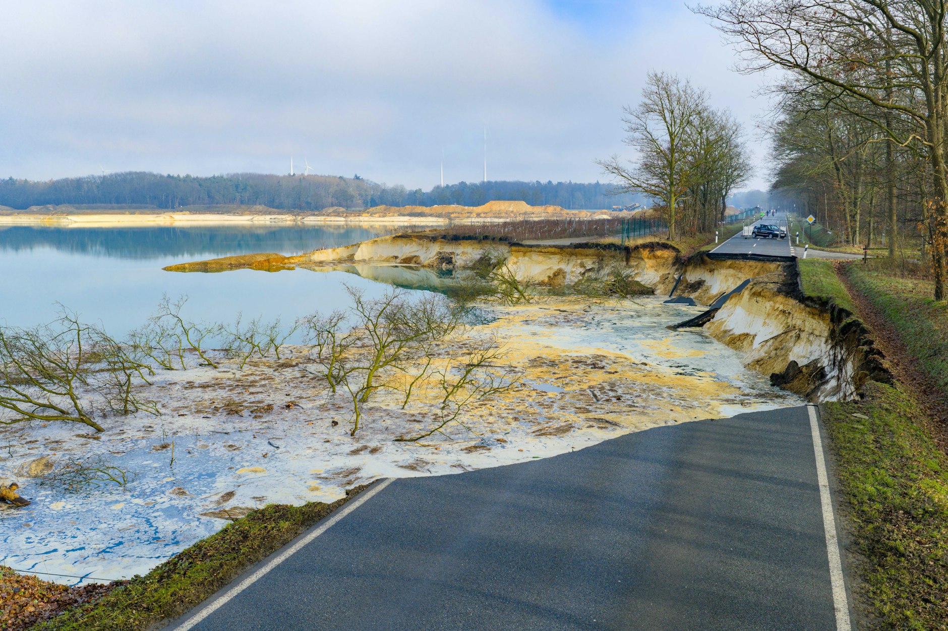 Direkt an einem Baggersee einer Quarzgrube sieht man den abgesackten Bereich der Straße, Teile des Asphalts liegen im Wasser.