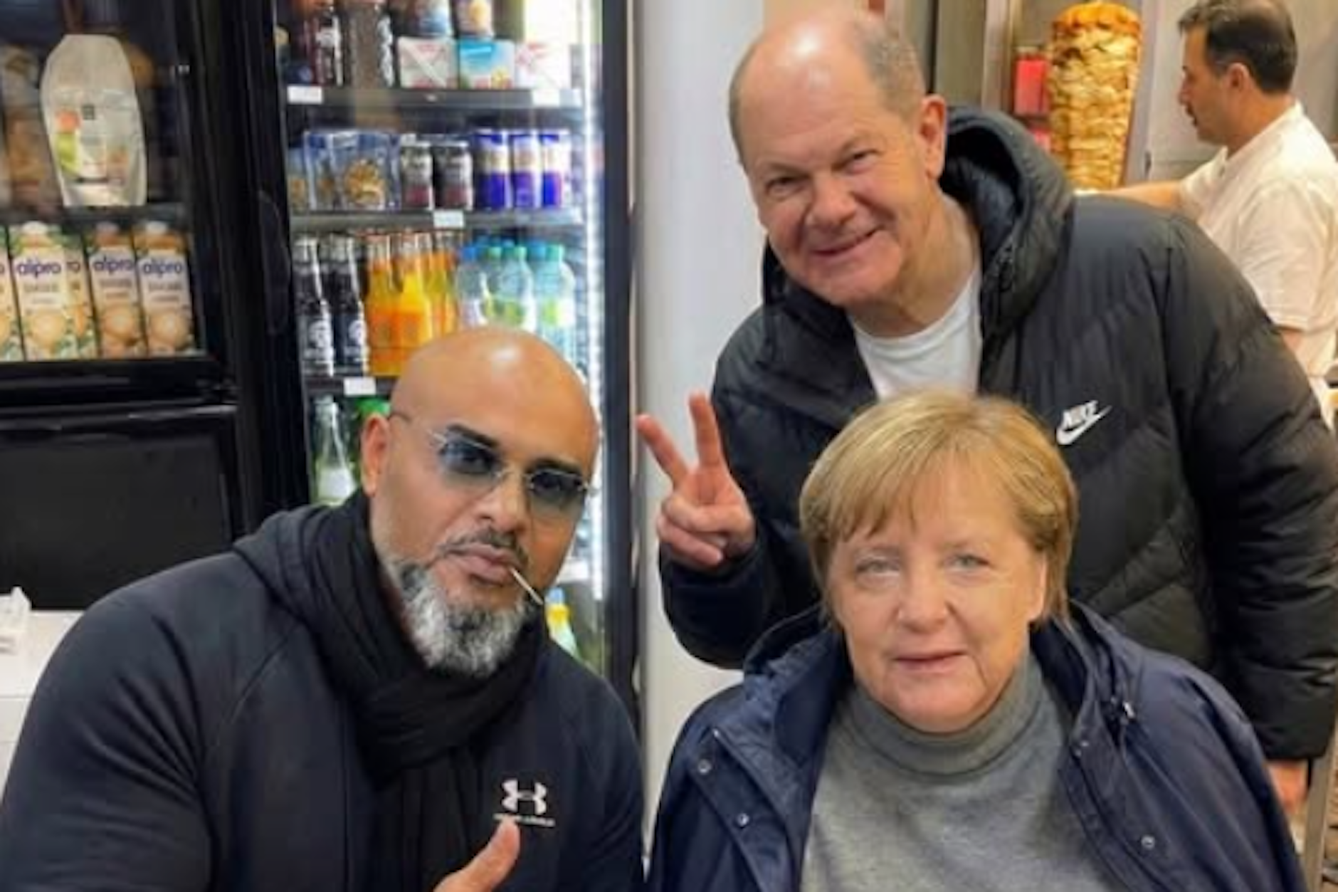 Was hat es mit diesem Foto von Rapper Massiv (l.) und den beiden Ex-Kanzlern Olaf Scholz und Angelo Merkel zu tun?