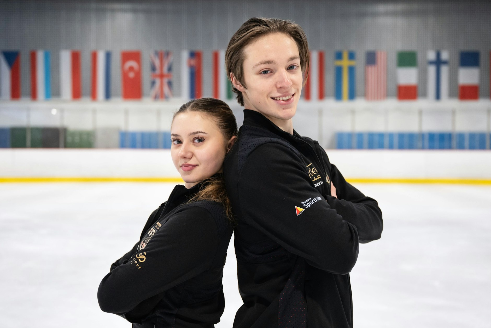 Die Eistänzer Alexia Kruk und Jan Eisenhaber vor den internationalen Fahnen, die die Eishalle in der Paul-Heyse-Straße schmücken.