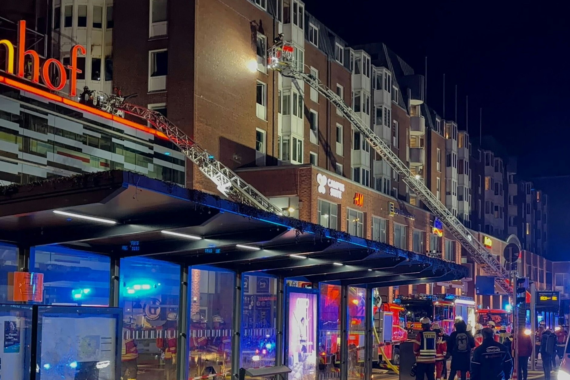 Einsatzkräfte der Feuerwehr arbeiten auf Drehleitern an einem Wohnhaus neben dem Einkaufszentrum Sophienhof in der Kieler Innenstadt, in dem am Abend ein Brand ausgebrochen war. 