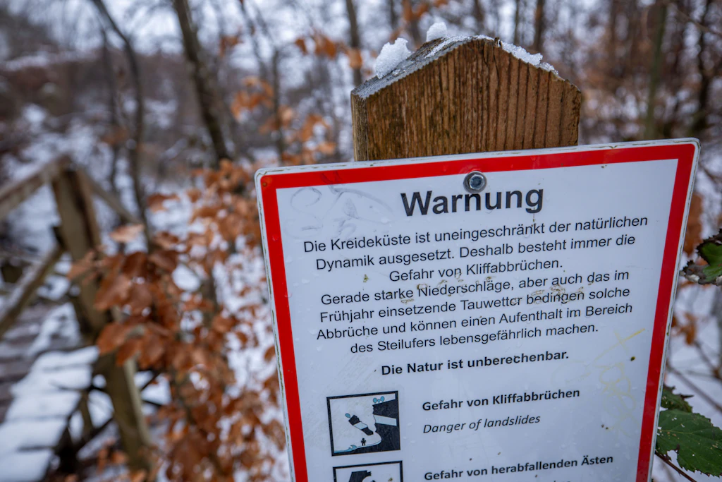 Ein Warnschild informiert über die Gefahren an der Steilküste am Ostseestrand auf der Insel Rügen.