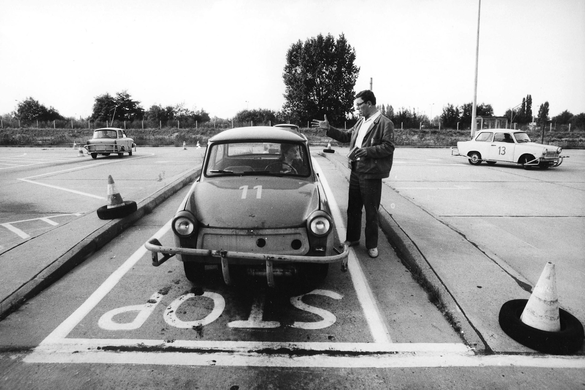 Fahrlehrer mit im Trabant sitzender Fahrschülerin auf einem Übungsgelände in der DDR.