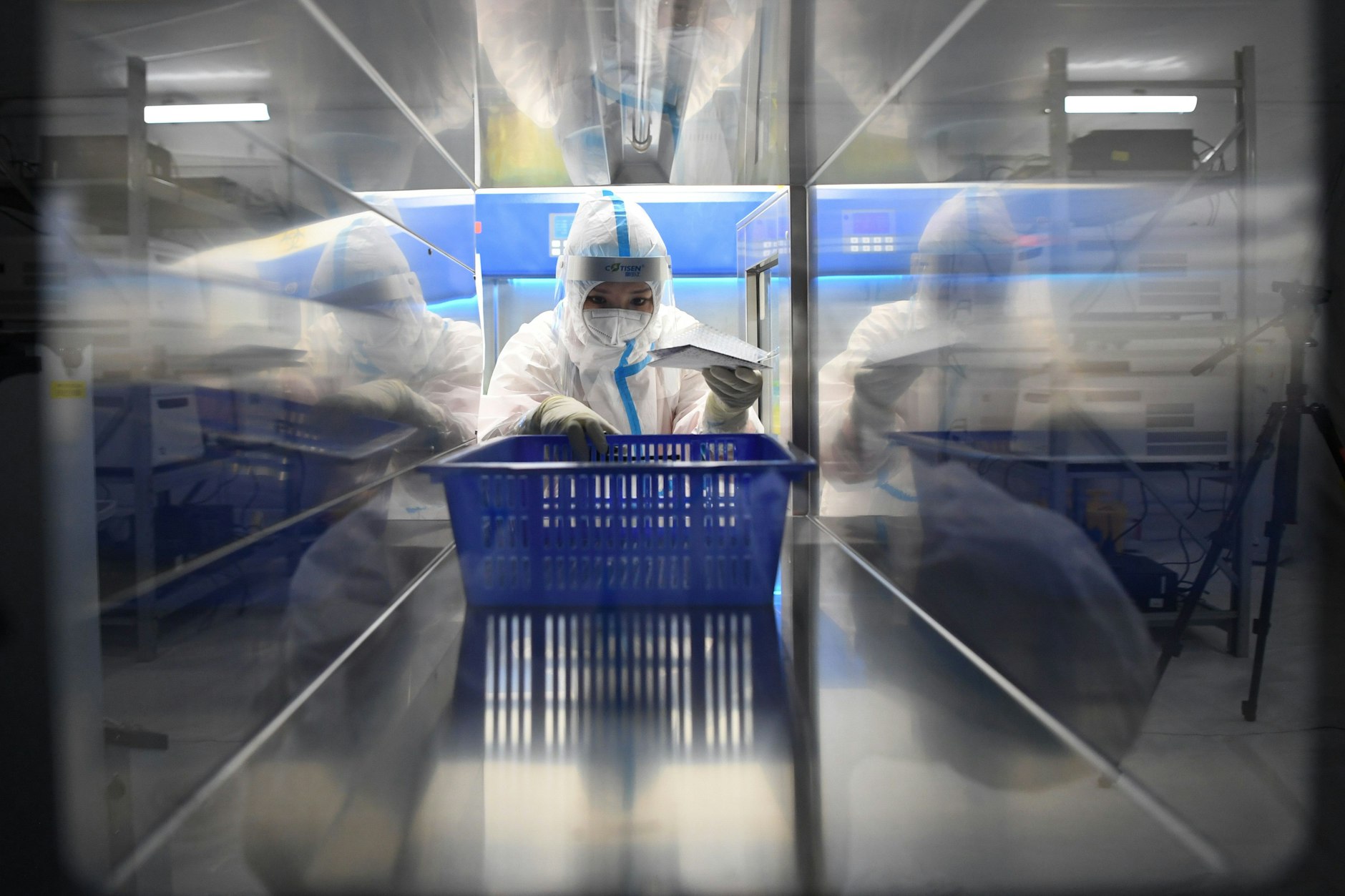 Eine medizinische Angestellte trägt einen Schutzanzug und hat einen blauen Korb in der Hand, während sie in einem Testlabor für Corona-Tests arbeitet.