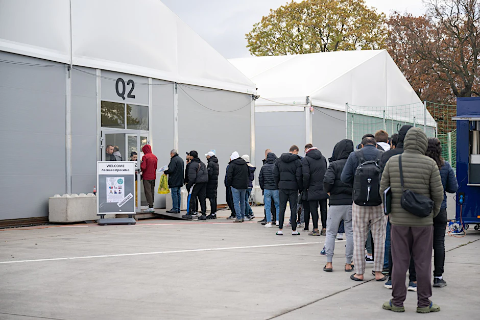 Am ehemaligen Flughafen Tegel stehen geflüchtete Menschen vor einer Leichtbauhalle.