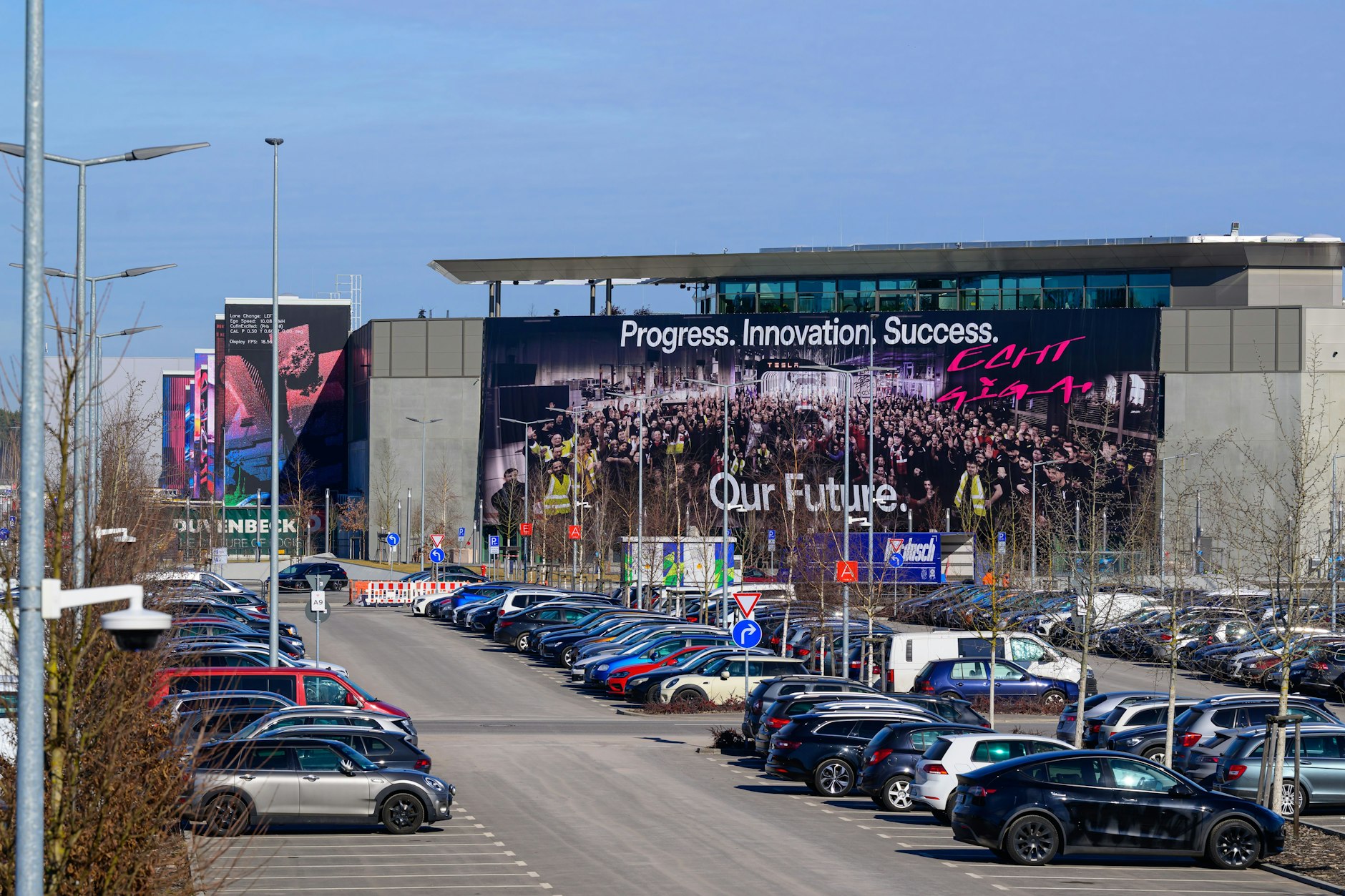 Ein riesiges Transparent (Progress. Innovation, Success. Our Future) hängt an der Fassade am Haupteingang der Tesla-Gigafactory Berlin-Brandenburg.