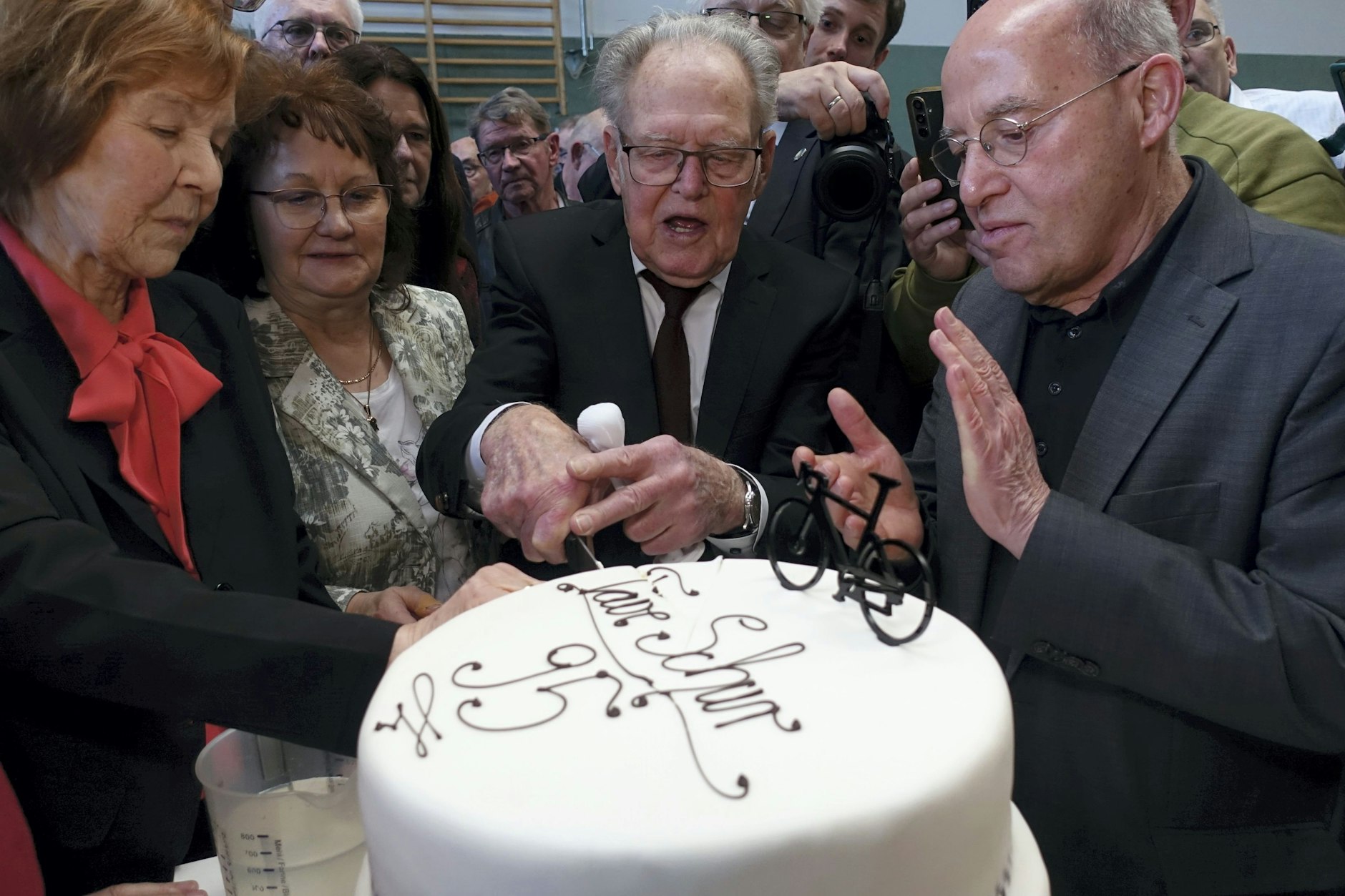 Täve Schur (2.v.r.) schneidet unter Applaus von Gregor Gysi (r.), Mitglied des Deutschen Bundestages, im Sportzentrum „Am Mühlberg“ in Kleinmühlingen eine dreistöckige Buttercreme-Torte mit einem Rennrad sowie der Aufschrift „Täve Schur 95“ an.
