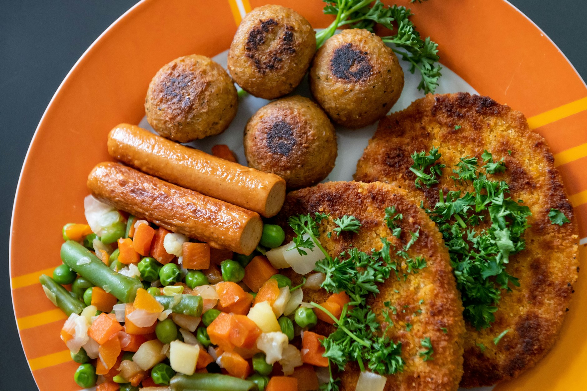 Vegane Falafel, vegane Schnitzel, vegane Würstchen und Gemüse sind auf einem Teller in einer Küche zu sehen.