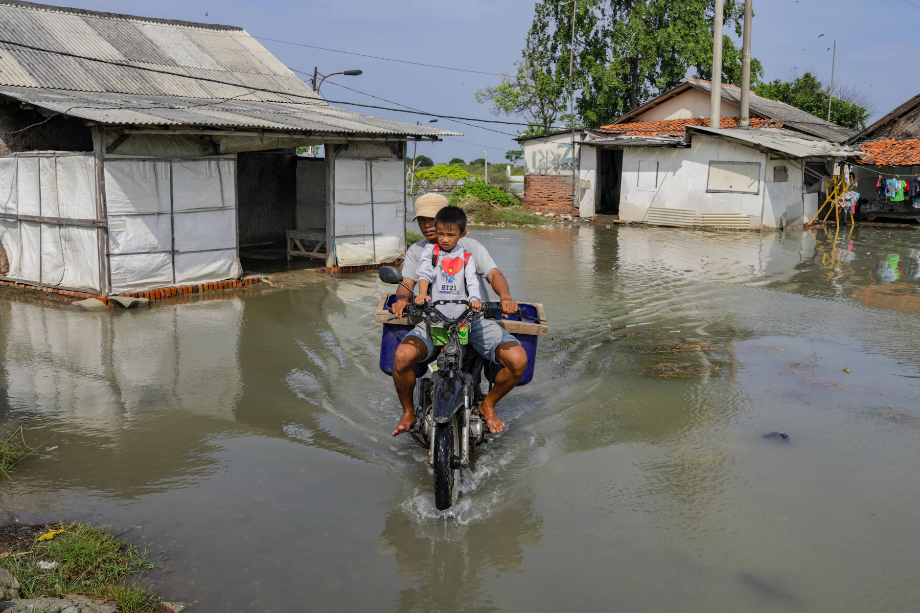 Ein Motorradfahrer fährt mit seinem Sohn über eine überflutete Straße im indonesischen Dorf Cemarajaya in Karawang, Westjava.