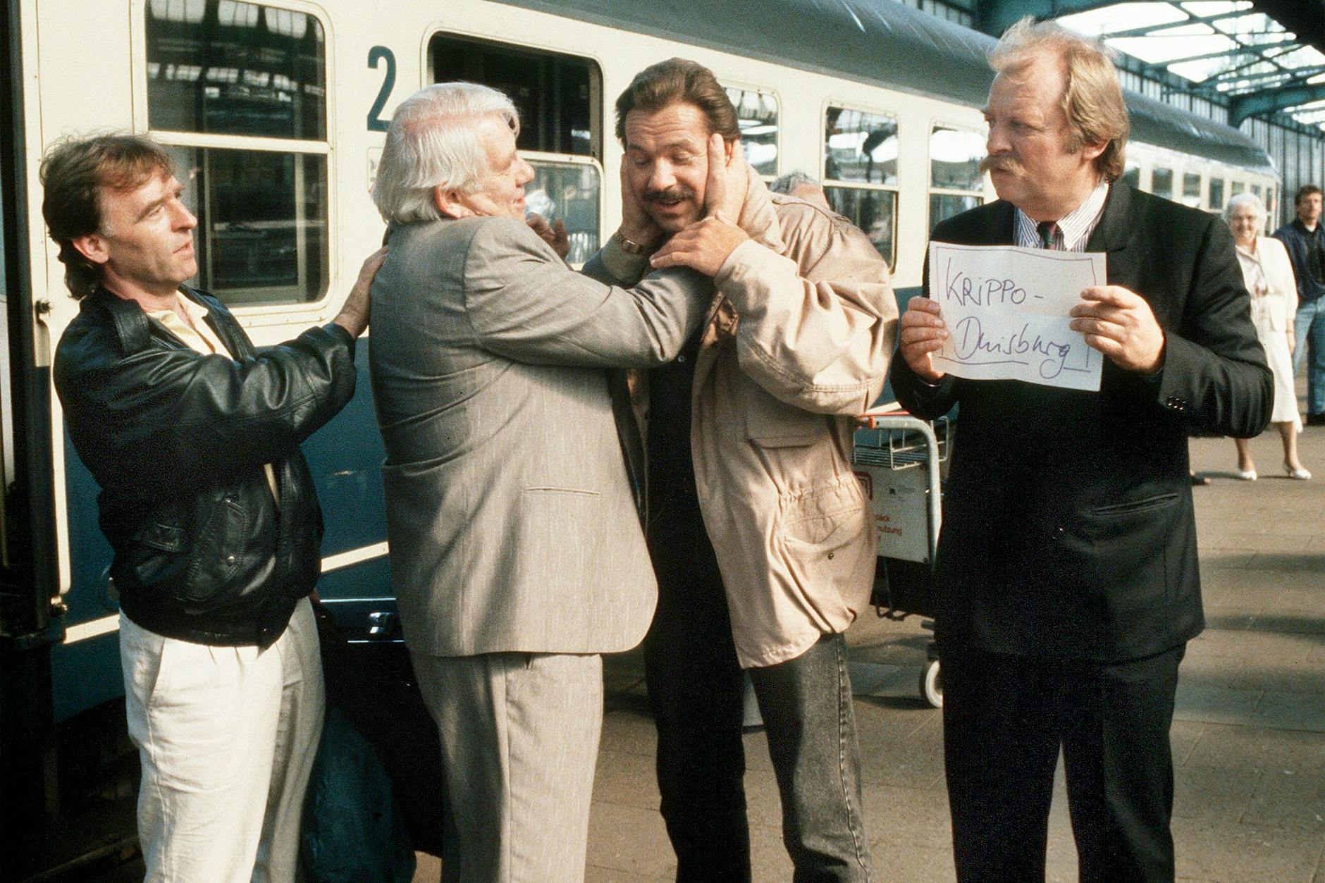 Die Folge „Unter Brüdern“ führte „Polizeiruf 110“ und „Tatort“ im Oktober 1990 zusammen. Thanner (Eberhard Feik, r.) und Schimanski (Götz George, 3.v.l.) nehmen die Kollegen Grawe ( Andreas Schmidt-Schaller, l.) und Fuchs (Peter Borgelt, 2.v.l.) aus Berlin-Ost am Duisburger Bahnhof in Empfang.