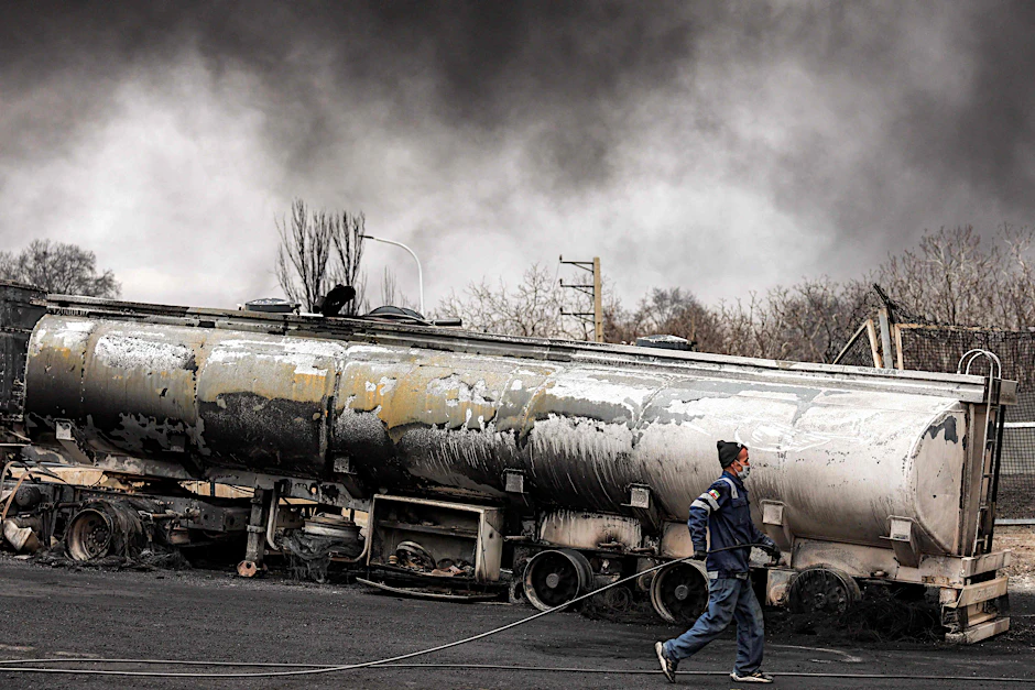 Ein Mitglied des iranischen Zivilschutzes mit einem Schlauch neben einem zerstörten Tankwagen in der Nähe eines noch immer brennenden Fahrzeugs nach einem nächtlichen Luftangriff auf die Shahran-Ölraffinerie im Nordwesten Teherans am 8. März 2026