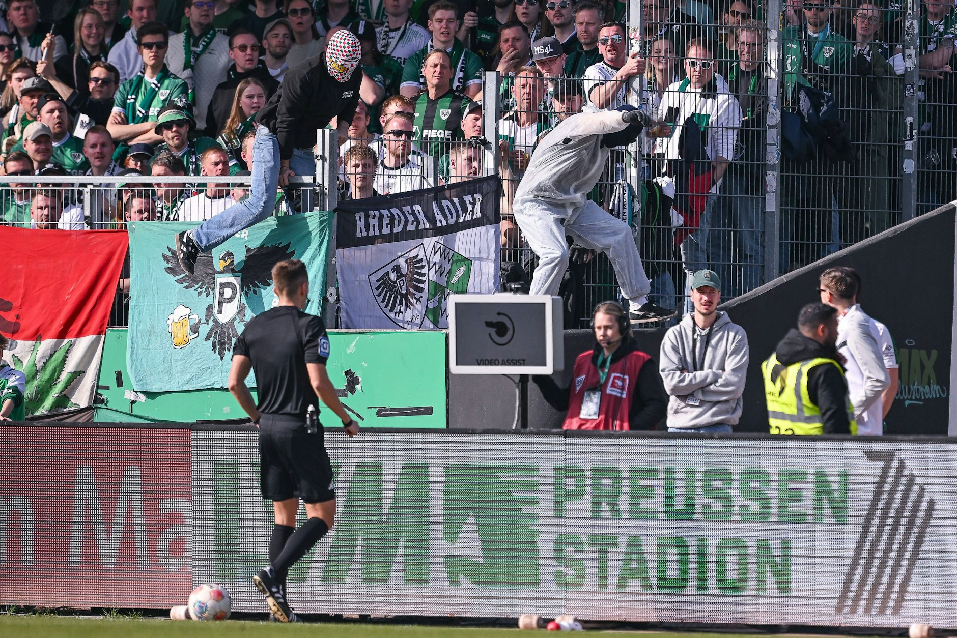 Auf dem Weg zum Spielfeldrand war für Schiedsrichter Felix Bickel der VAR-Monitor noch eingeschaltet – im Hintergrund aber sieht man den vermummten Fan, der im Spiel zwischen Preußen Münster und Hertha BSC den Netzstecker zog.