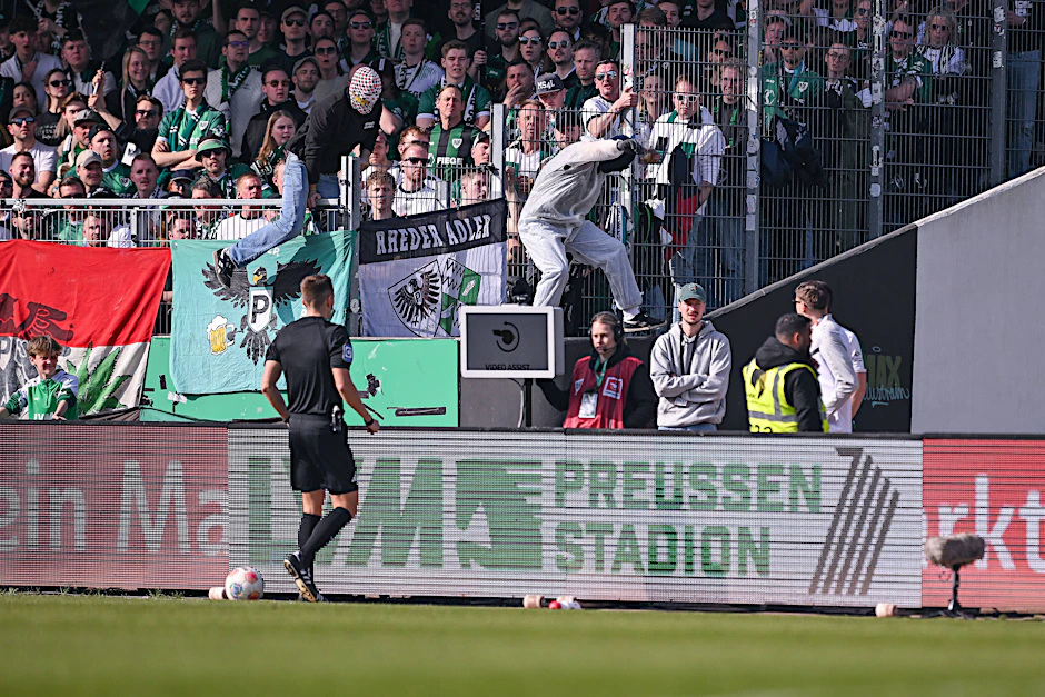 Auf dem Weg zum Spielfeldrand war für Schiedsrichter Felix Bickel der VAR-Monitor noch eingeschaltet – im Hintergrund aber sieht man den vermummten Fan, der im Spiel zwischen Preußen Münster und Hertha BSC den Netzstecker zog.