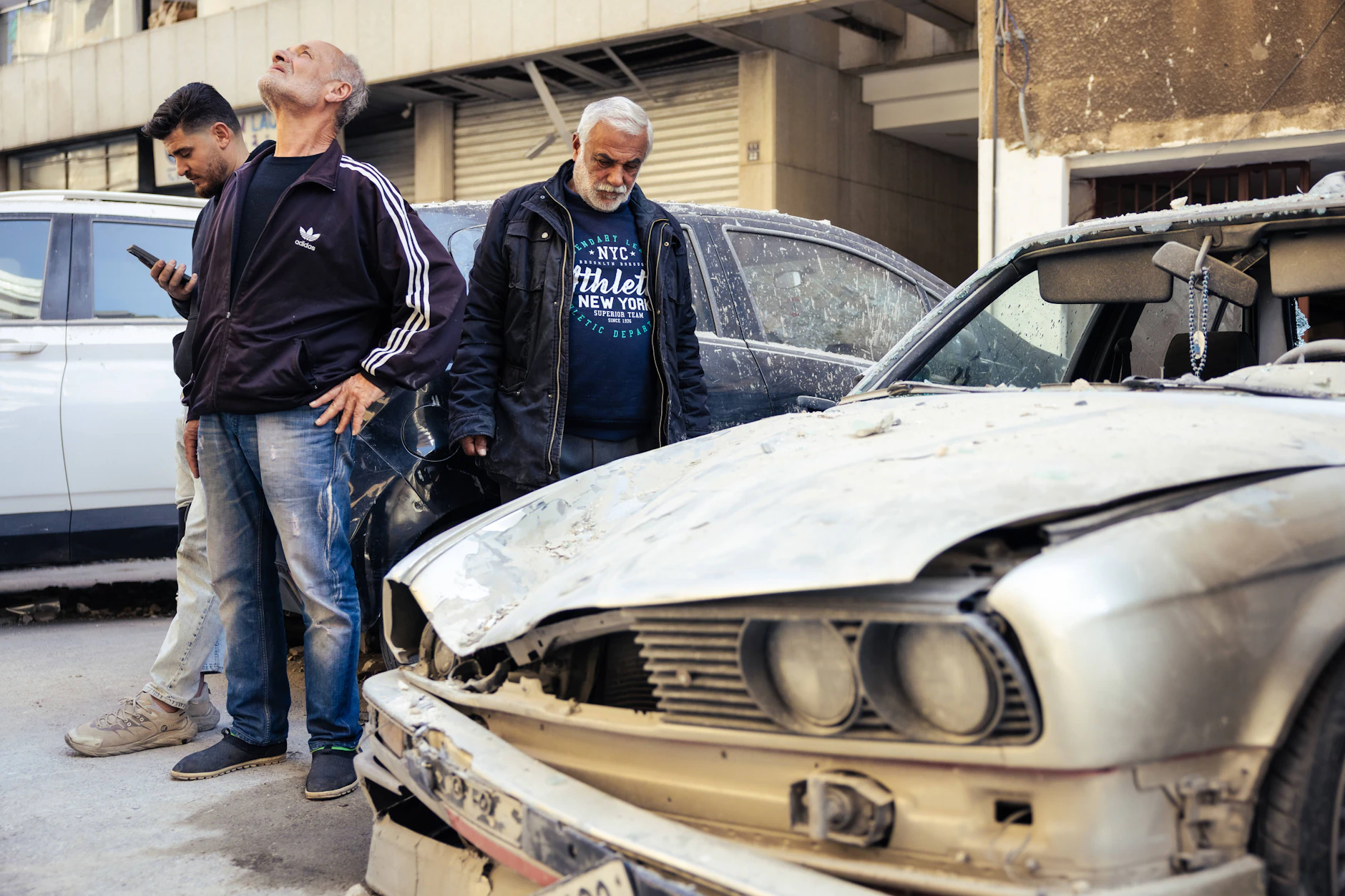 Im Stadtteil Aicha Bakkar stehen drei Männer zwischen demolierten Autos.